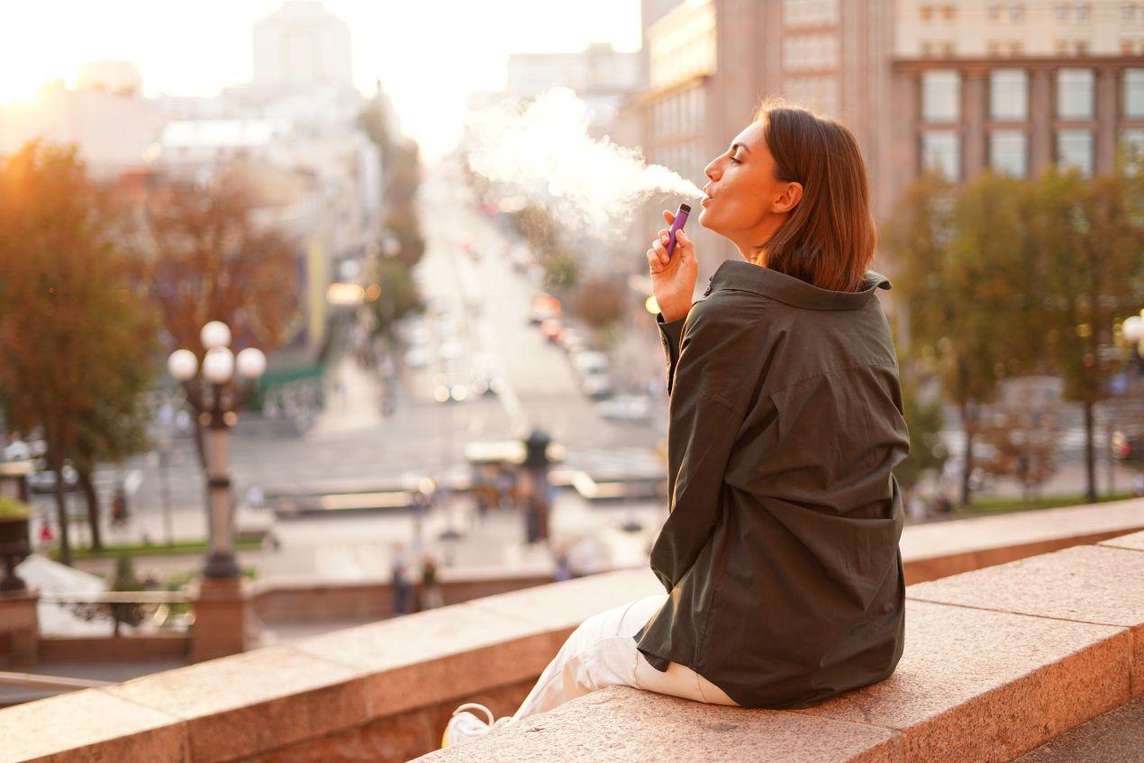 Eine Frau nutzt ein vape im urbanen Raum und genießt den Moment – Beispiel für neue Konsumrituale im Alltag durch smarte Produkte.
